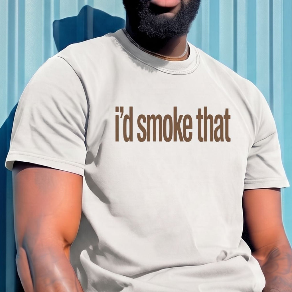 A man wearing a light beige bucket hat, sunglasses, and a matching light beige t-shirt with the text 'i'd smoke that' printed in brown across the chest, sitting against a blue corrugated metal wall.