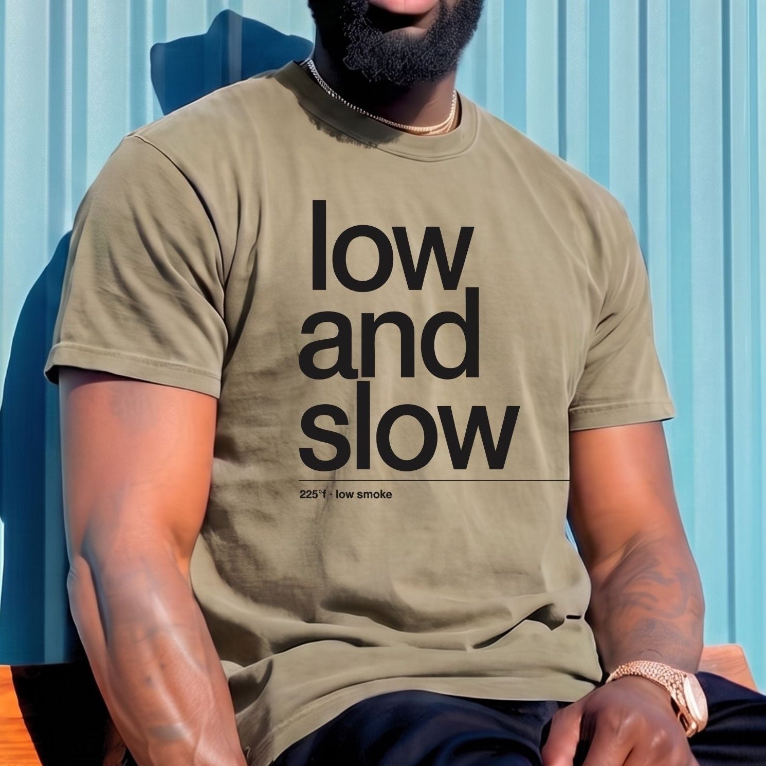 A man wearing a beige bucket hat, sunglasses, and a beige t-shirt with the text 'low and slow' in black, sitting against a blue corrugated metal wall.