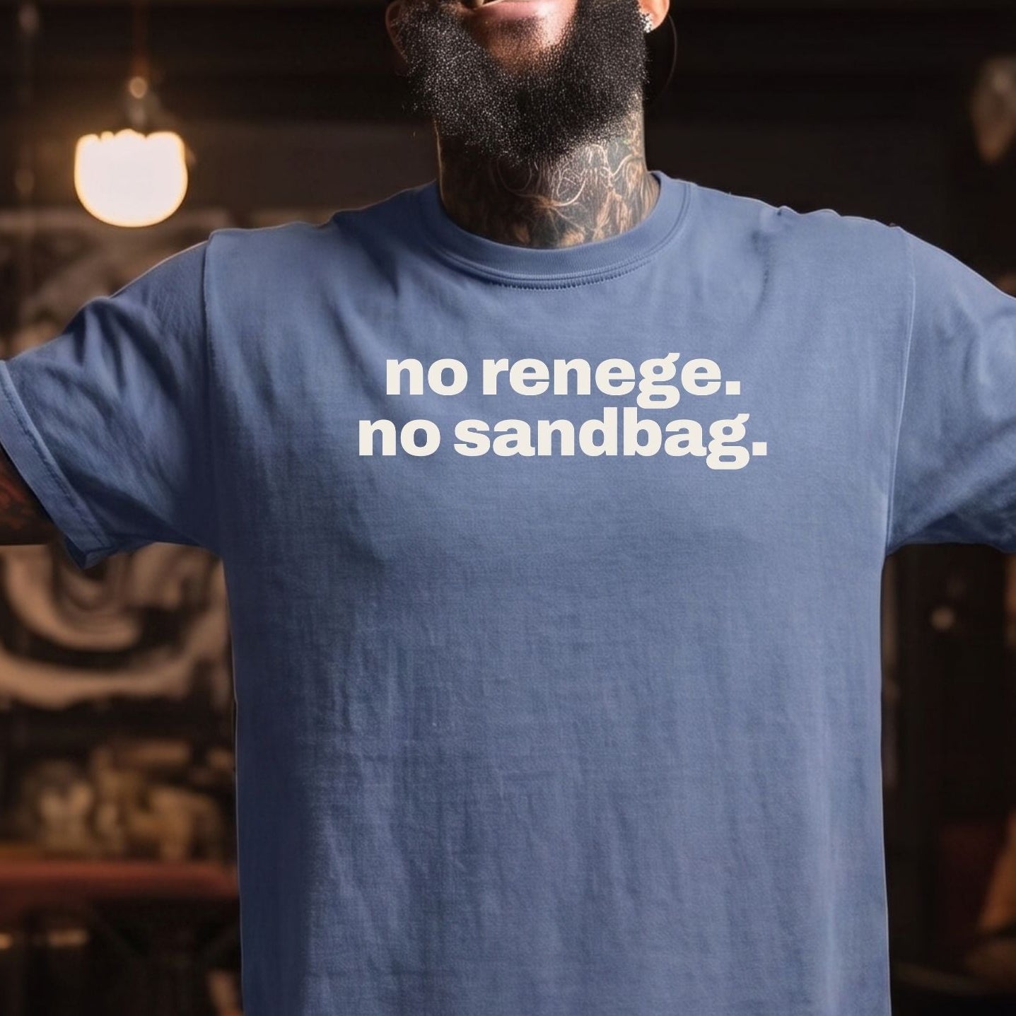 A smiling man with a beard and tattoos wearing a spades blue t-shirt with the white printed text 'no renegade. no sandbag.